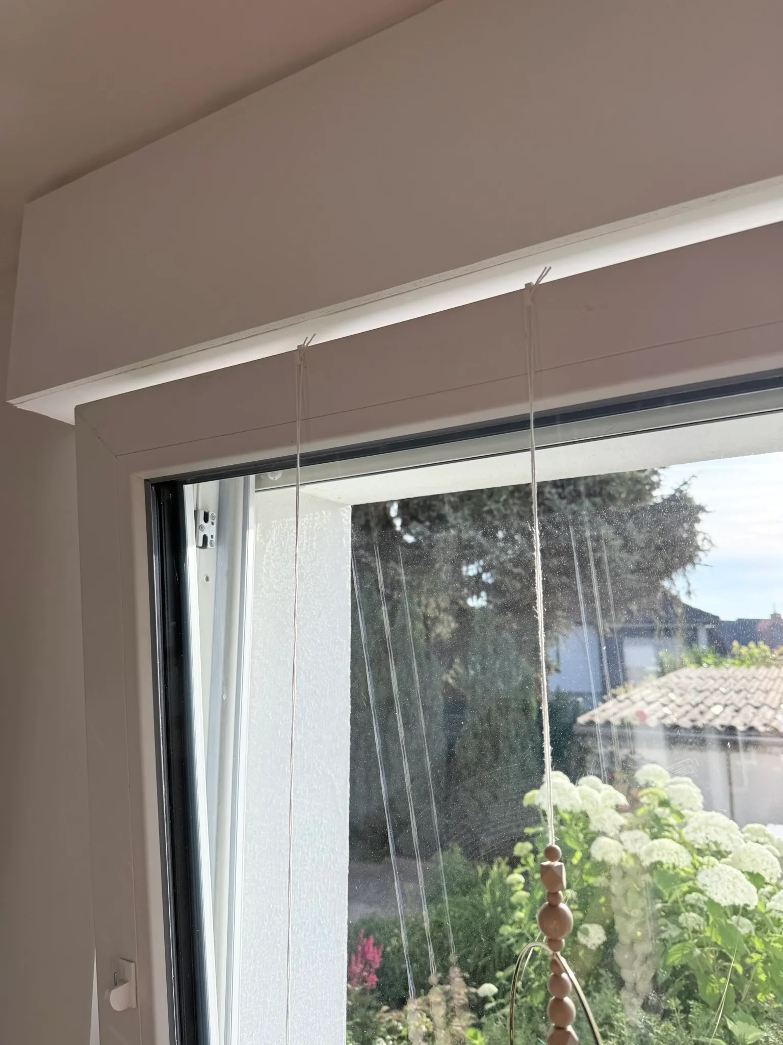 Weiße Fensterhaken über dem Fensterflügel, daran hängt Deko an dünnen Schnüren
